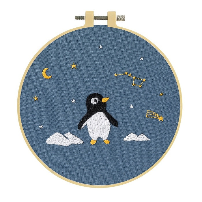 Embroidery hoop with a penguin, moon and stars on blue fabric.
