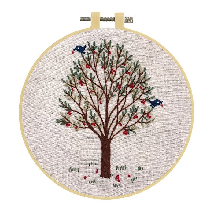 Embroidery hoop with two birds in a leafy tree on natural fabric.