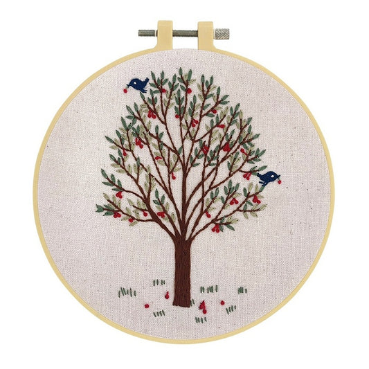 Embroidery hoop with two birds in a leafy tree on natural fabric.
