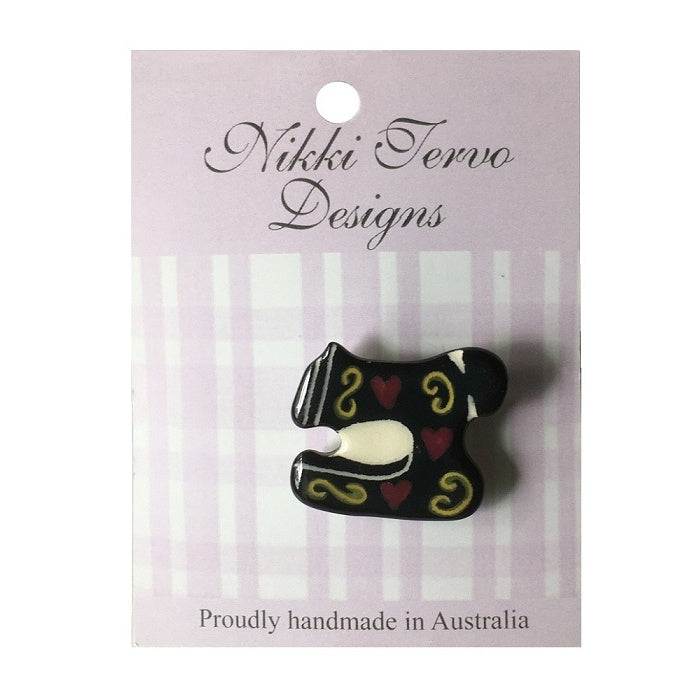Black ceramic sewing machine brooch with gold swirls and red hearts.