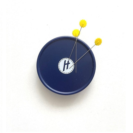 Round, navy pin holder with yellow pins.