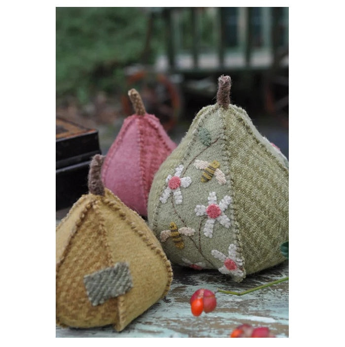 Three embroidered fabric pears on a rusitc wooden surface.
