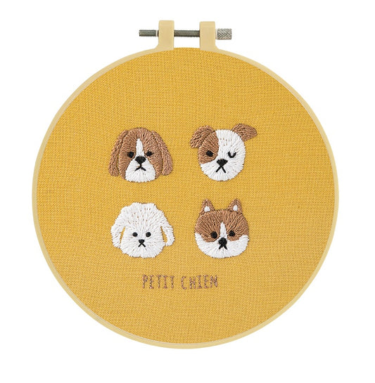Embroidery hoop with four puppy faces on a mustard yellow background.