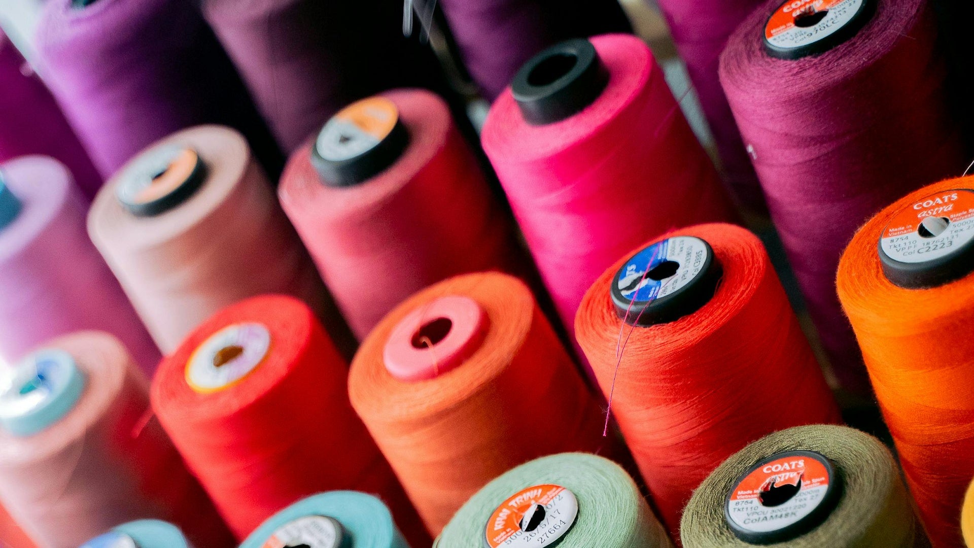 Close-up of colourful cones of sewing thread arranged rows.