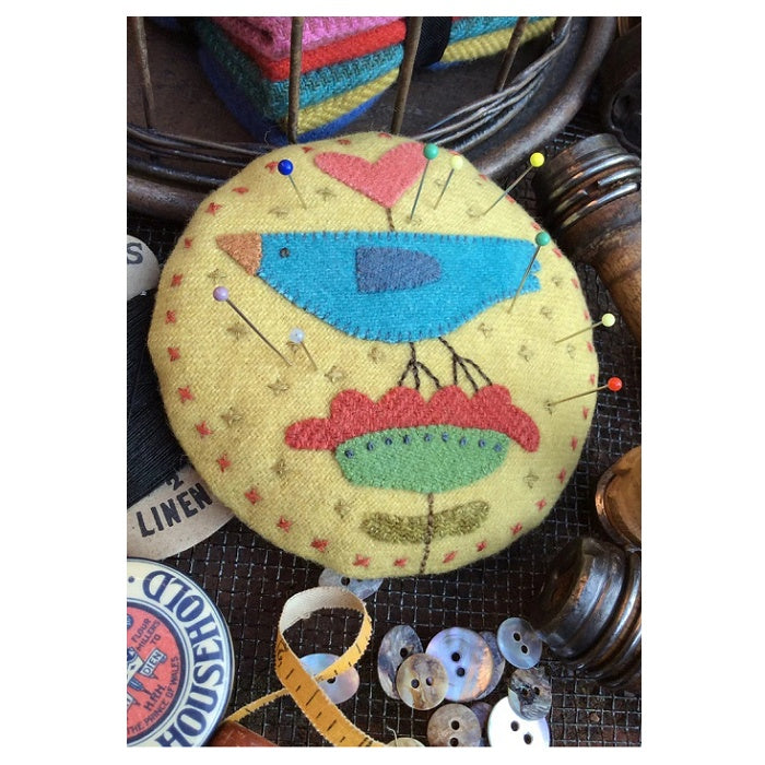 Round fabric pin cushion with colourful bird on a flower.