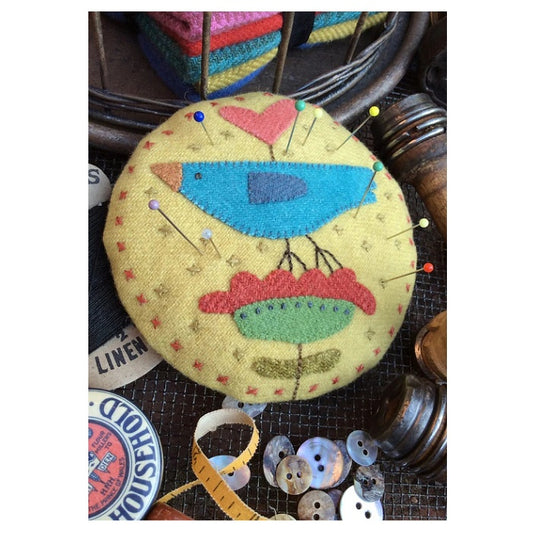 Round fabric pin cushion with colourful bird on a flower.