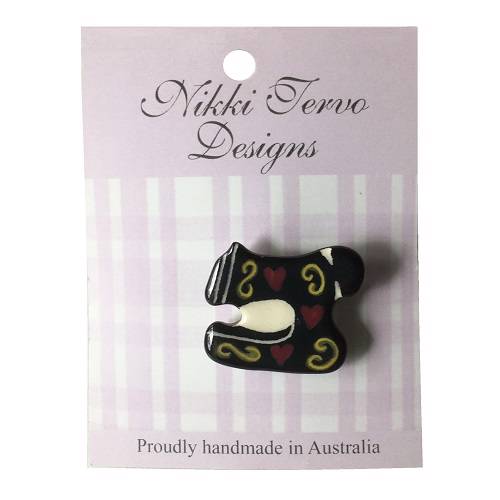 Black ceramic sewing machine brooch with gold swirls and red hearts.