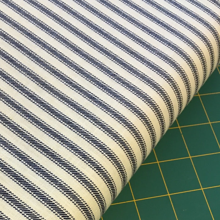Roll of navy and cream striped fabric on a cutting mat.